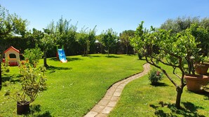 A grassy backyard with a stone pathway, a small playhouse, and a slide. - Terraced house a stone's throw from the sea (Capalbio Scalo)