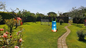 A well-maintained garden with a clear pathway, a colorful slide, and a small building with a red roof. - Terraced house a stone's throw from the sea (Capalbio Scalo)