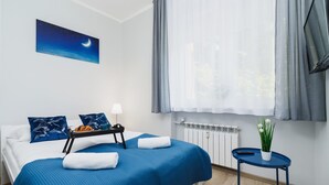 A neatly arranged bedroom with a bed, a bedside table with a tray, a potted plant, and a window with curtains.