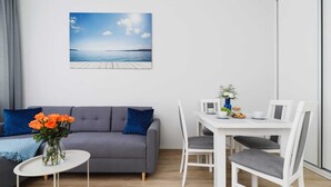 A modern living room with a grey sofa, a small white table, and a dining area with white chairs.