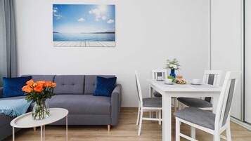 A modern living room with a grey sofa, a small white table, and a dining area with white chairs.