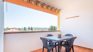 Un balcón con mesa y sillas, vistas al campo y suelo de baldosas.