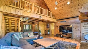 En rummelig opholdsstue med en stor sofa, et sofabord og et fjernsyn. En trætrappe fører op til en etage ovenpå.