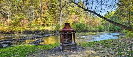 A rustic wooden structure in a forested area near a stream.