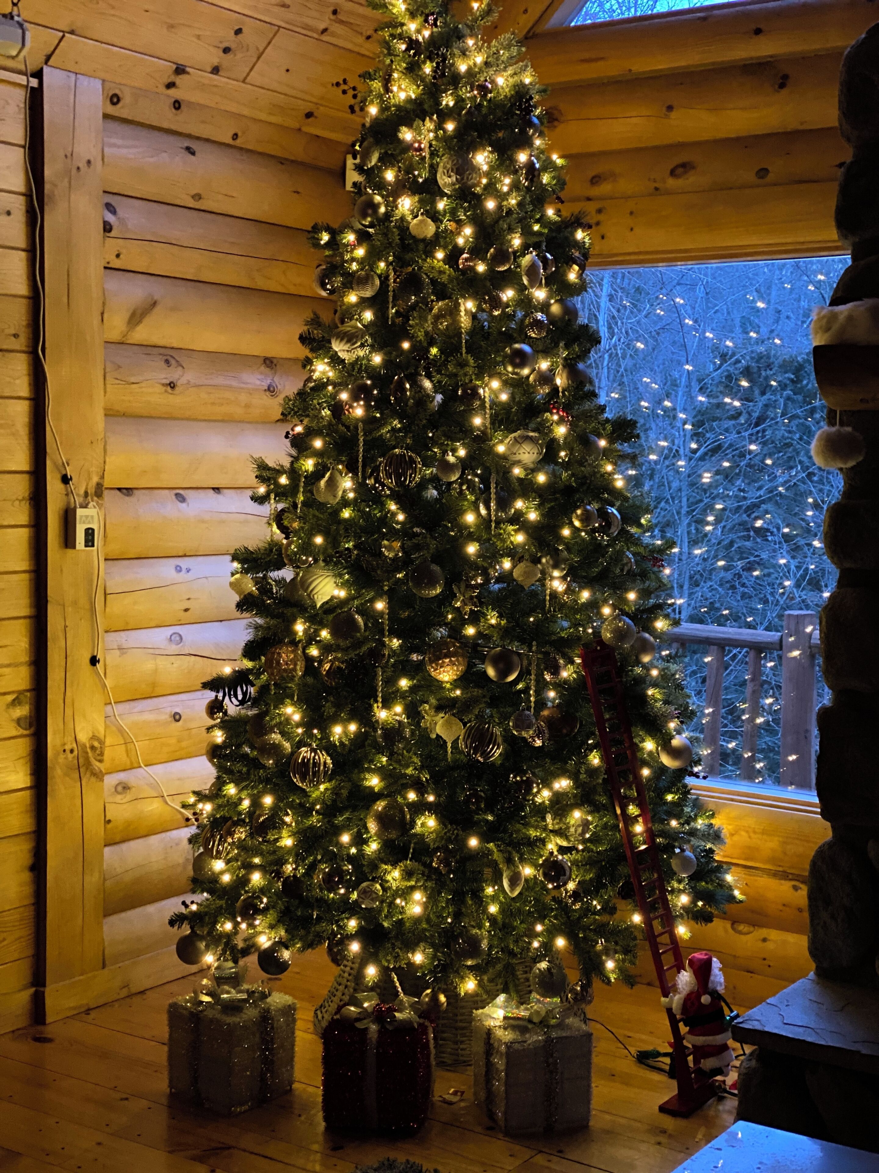 Árvore de Natal enfeitada com luzes e adornos dentro de uma cabana de madeira.
