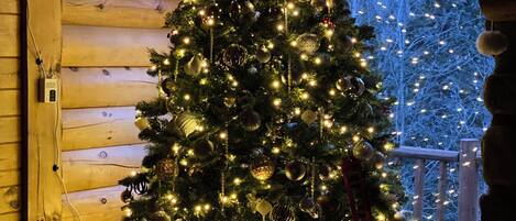Árvore de Natal enfeitada com luzes e adornos dentro de uma cabana de madeira.