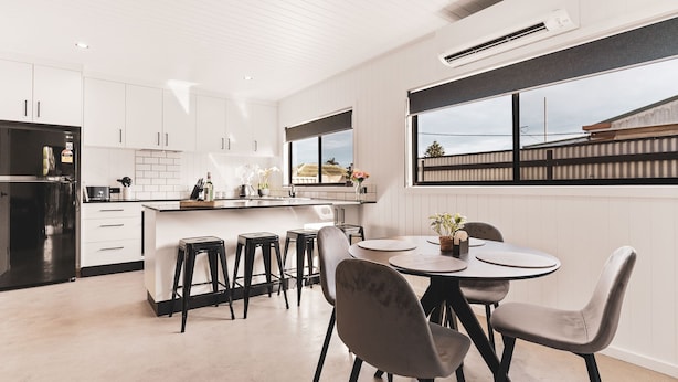 Una cocina moderna con armarios blancos, un refrigerador negro y una zona de comedor con una mesa redonda y cuatro sillas.
