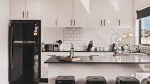 Una cocina moderna con armarios blancos, un refrigerador negro, una cafetera y una pequeña isla con taburetes.