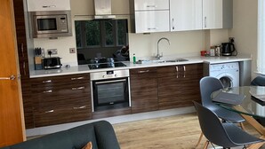 A compact kitchen with a microwave, oven, and dishwasher. There is a dining area with a table and chairs. - Aspire Apartments (York)