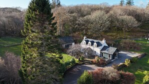 Une maison avec un chemin de pierre menant à une allée, entourée d’arbres et d’un champ d’herbe.