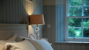 Une chambre à coucher avec un lit, une lampe, une fenêtre donnant sur un paysage verdoyant et une porte avec une serrure.