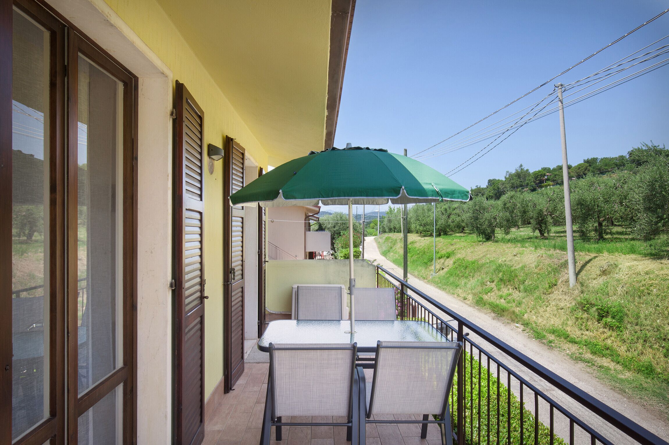 A balcony with a table and chairs, a green umbrella, and a view of a green landscape.