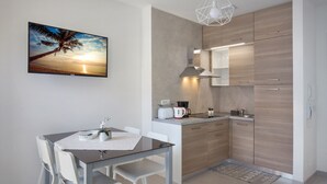 Une cuisine moderne avec des meubles en bois, un four encastré et un coin repas comprenant une table en verre et des chaises blanches.