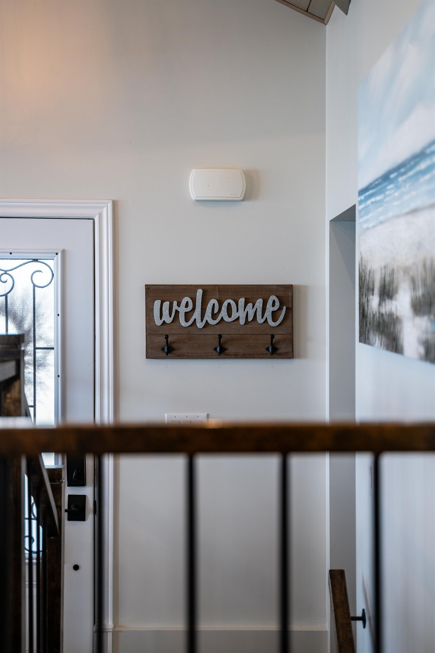 Un escalier avec une rampe en bois, une pancarte « Bienvenue » accrochée au mur et un tableau au-dessus.