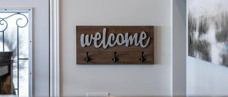 Un escalier avec une rampe en bois, une pancarte « Bienvenue » accrochée au mur et un tableau au-dessus.
