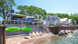 A waterfront property with a wooden deck, a covered seating area, and a sandy beach. - Lake Erie Luxury Retreat  Hot Tub + Private Beach + Sunset Views (Leamington)