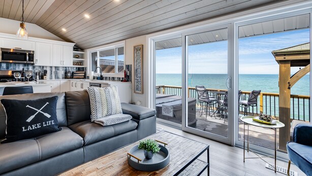 A modern kitchen with white cabinets, a stainless steel microwave, and a large window overlooking the ocean. - Lake Erie Luxury Retreat  Hot Tub + Private Beach + Sunset Views (Leamington)