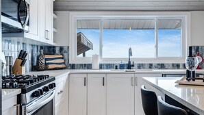 A modern kitchen with white cabinets, a wooden floor, and a large window offering a view. - Lake Erie Luxury Retreat  Hot Tub + Private Beach + Sunset Views (Leamington)