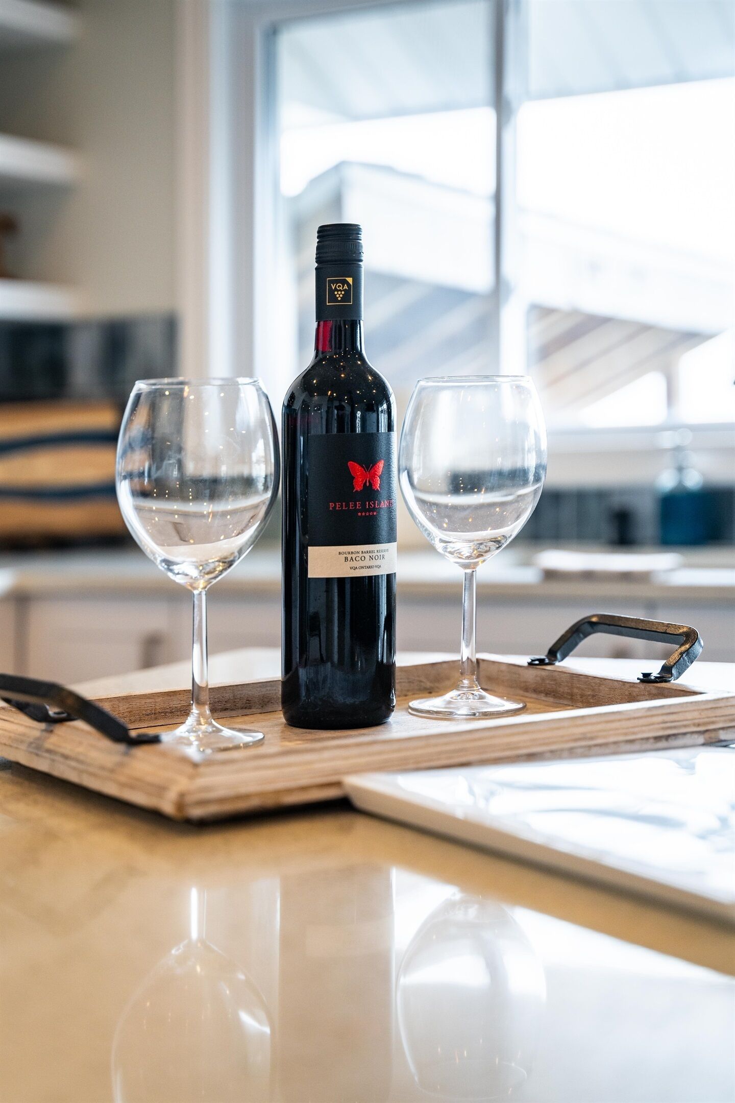 Una botella de vino y dos copas sobre una bandeja de madera en una cocina.