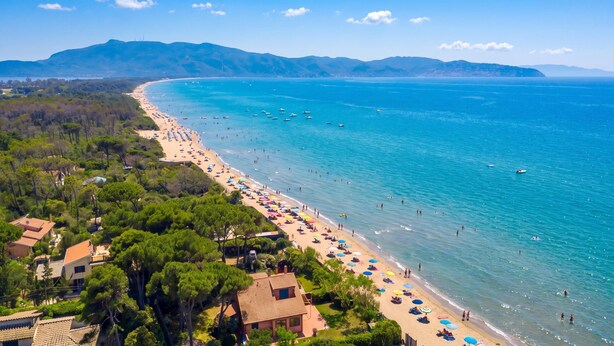 A coastal beach with clear blue waters, a sandy shore, and a backdrop of green hills. - Casa Giannellina (Orbetello)