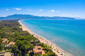 A coastal beach with clear blue waters, a sandy shore, and a backdrop of green hills.