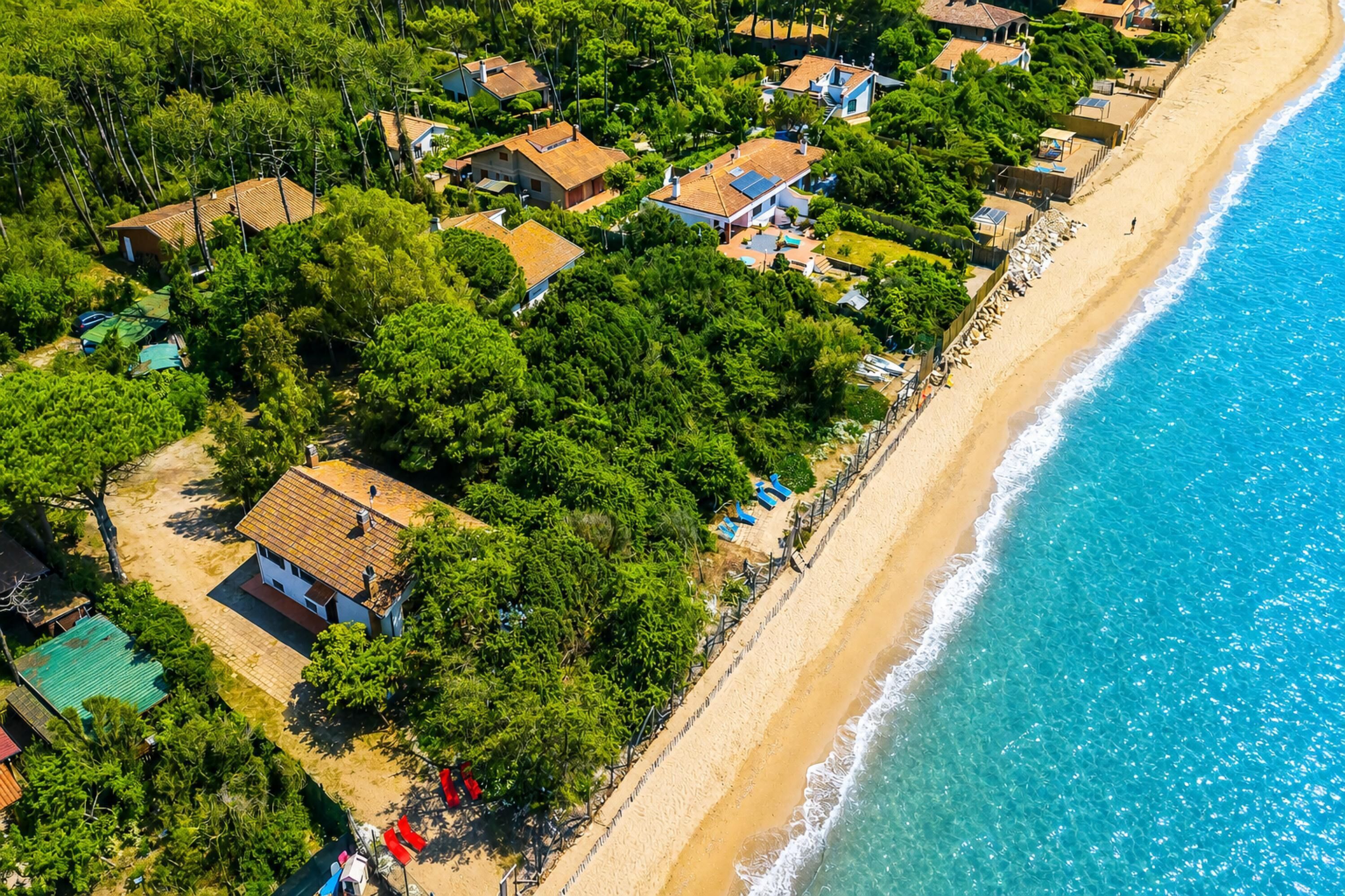 An aerial view of a coastal residential area with houses, a beach, and a clear blue sea.