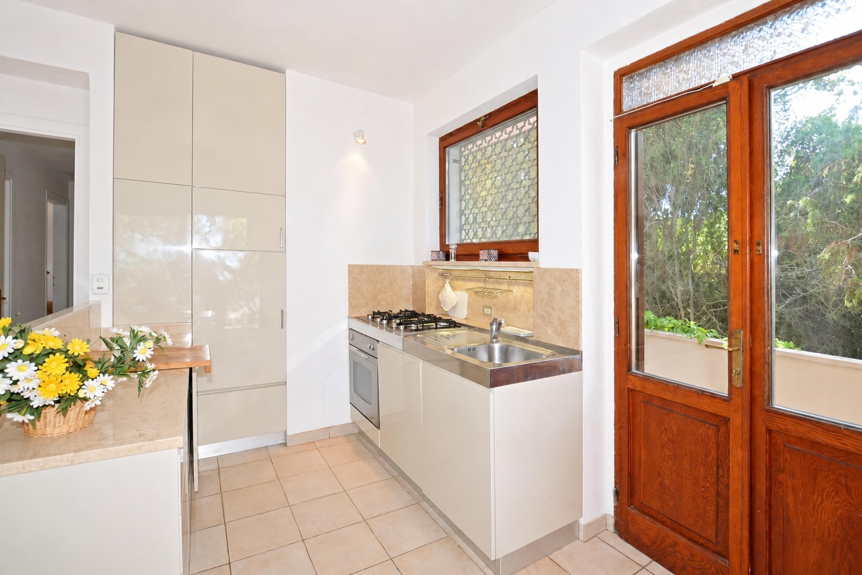 Una cocina moderna con estufa integrada, pileta y puerta de madera con paneles de vidrio.