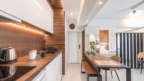 Una cocina moderna con encimera de madera, hervidor y cafetera. Hay una zona de comedor con una mesa y sillas.