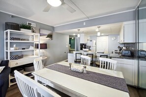 Una cocina moderna con armarios blancos, un comedor con mesa blanca y una sala de estar con sofá y televisor.