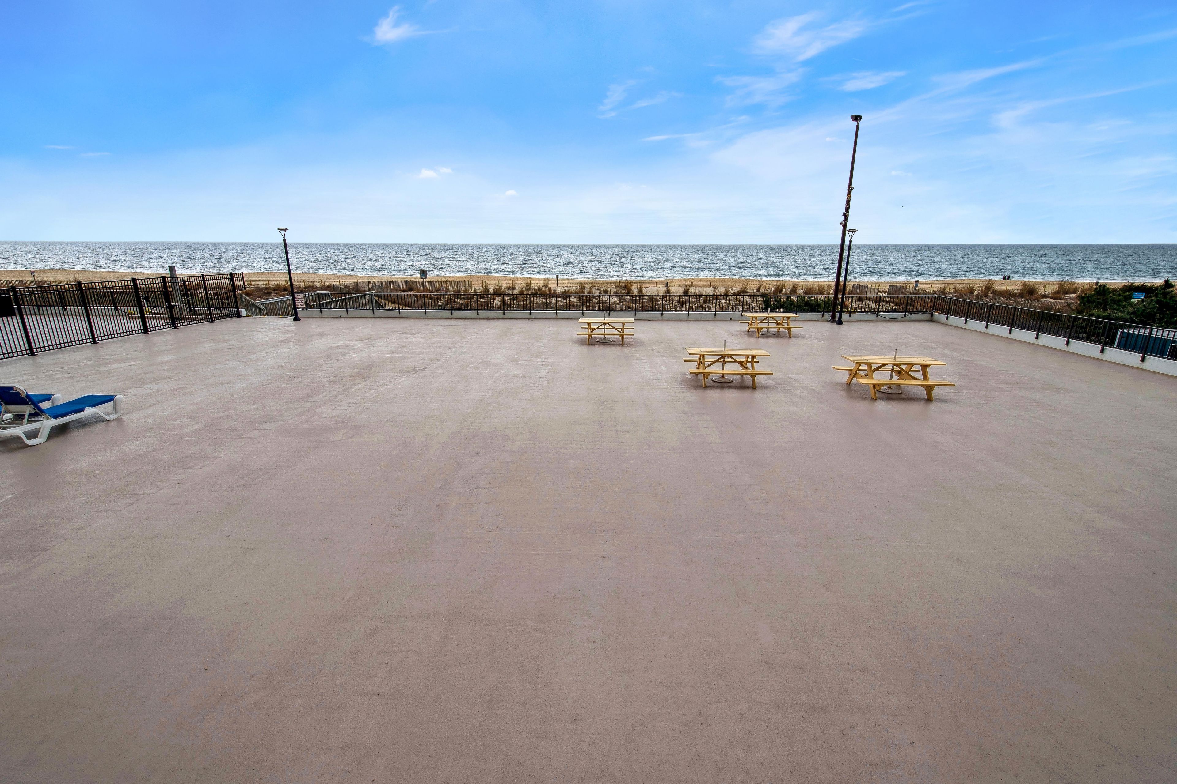 Un espacio al aire libre vacío con mesas de picnic, una valla y vista a la playa.