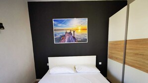 Hotellihuone, jossa on sänky, valkoiset vuodevaatteet, maalaus, jossa on kuvattu auringonlasku laiturin yllä, ja puupaneeli seinässä.