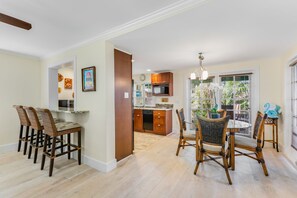 A kitchen with a dining area, wooden chairs, a round table, and a view of the outdoors. - SAILOR HOUSE ~ Charming 2 Bedroom, 1.5 Bathroom Just Steps to Duval St! (Key West)