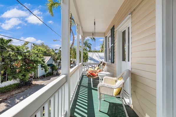 Relax on the porch with a view of the surrounding neighborhood, featuring a green floor and comfortable wicker chairs.