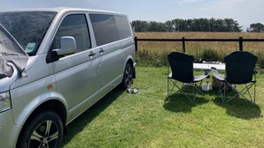 A white van parked on a grassy field with two black folding chairs and a table. - Pembs Campervan VW T5 Travel and Stay in Style (Haverfordwest)