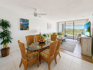 A dining area with wicker chairs and a glass table, a green sofa, and a TV on a wooden cabinet. - Sea Haven Delight A delight in Key West Open January & February 2027 (Key West)