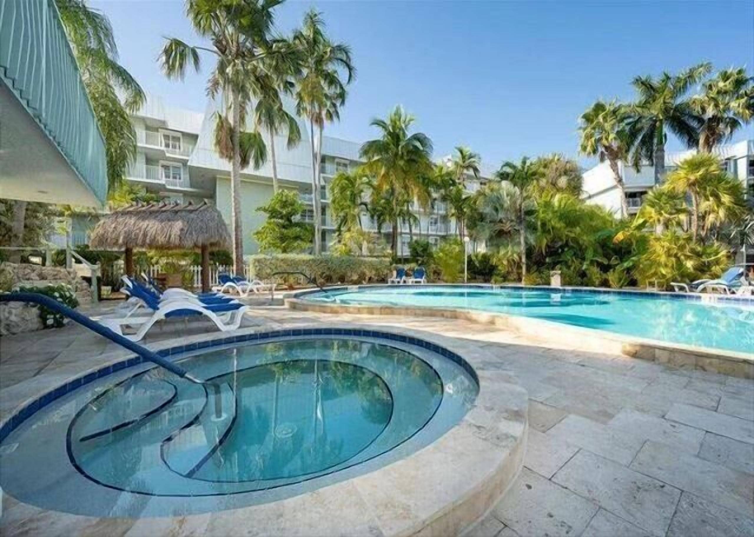 Ein Poolbereich mit Liegestühlen, einem Whirlpool und Palmen.