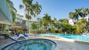 Un área de piscina con sillones de descanso, una bañera de hidromasaje y palmeras.