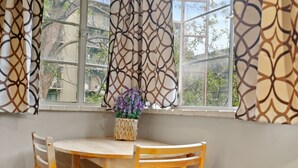 Ein Essbereich mit einem runden Tisch, Holzstühlen, einer Vase mit violetten Blumen und gemusterten Vorhängen.