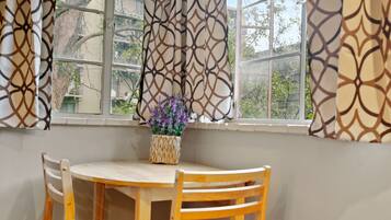 Un coin repas avec une table ronde et des chaises en bois, un vase rempli de fleurs violettes et des rideaux à motifs.