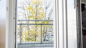 A view from a balcony with a metal railing, looking out onto a street with parked cars and trees with yellow leaves.