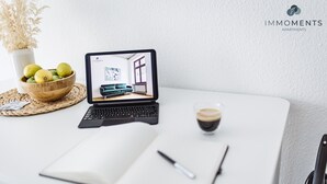 A laptop displaying an interior view of a room with a blue sofa, a coffee cup, and a bowl of fruit on a table.
