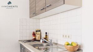 A modern kitchen with white tiles, stainless steel appliances, and wooden cabinets.