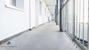 A corridor with a bicycle leaning against the wall, white walls, and a metal railing on the right.