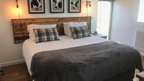 A bedroom with a wooden headboard, a large bed with white bedding and plaid pillows, and three framed cow paintings on the wall. - Hot Tub*,Fire, Super-king , Zip n Link beds.Views (PRESTON)