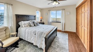 A bedroom with a bed, a chair, a nightstand, a lamp, a ceiling fan, and a view of the outdoors. -  Cabin with Jaw-dropping Views near Black Canyon (Crawford)