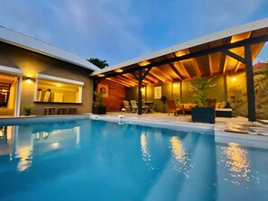 An outdoor swimming pool with a covered patio area, seating, and a stone wall.