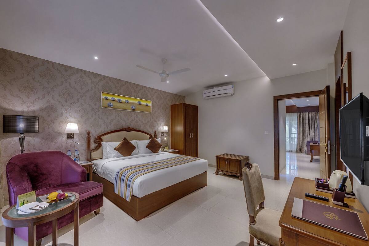 A hotel room with a bed, a desk, a chair, a TV, and a ceiling fan.