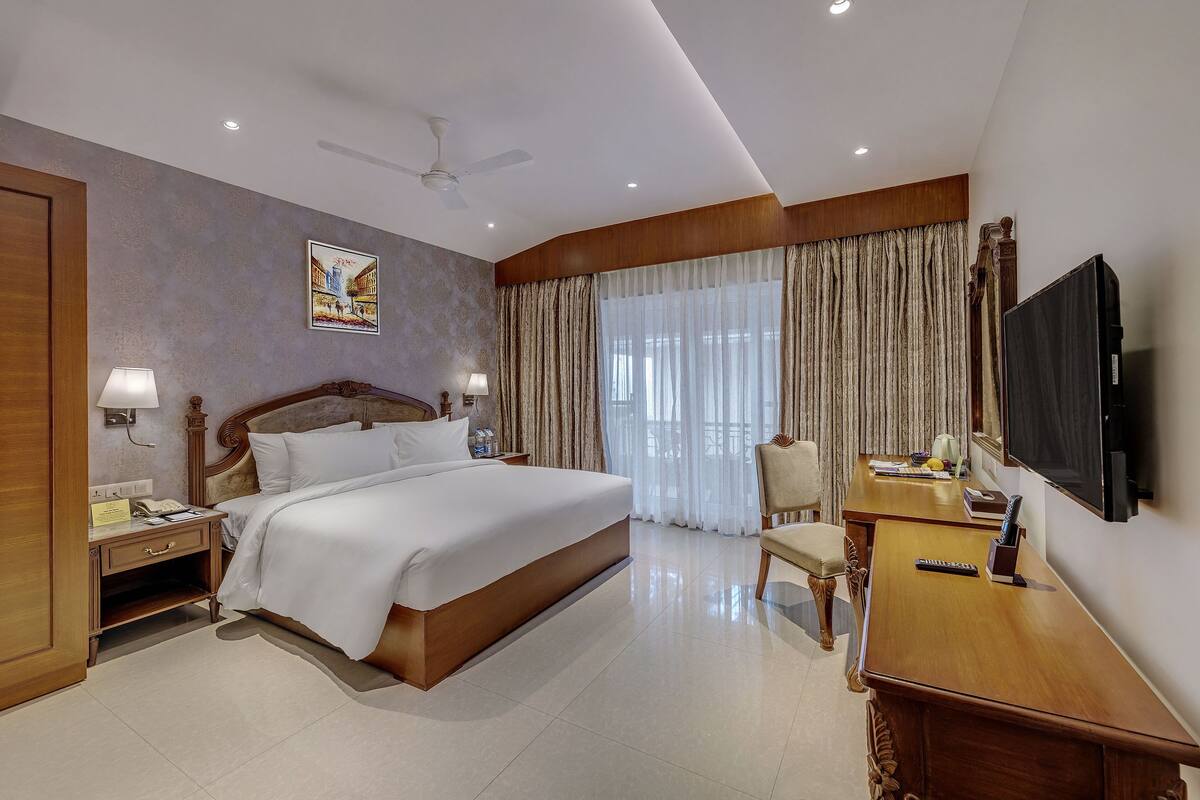 A hotel room with a large bed, a desk with a TV, a chair, and a ceiling fan.