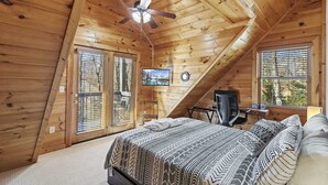 A cozy attic bedroom with a bed, a desk, and a TV. - Modern Lodge | Hot Tub | EV Charger | Near Blue Ridge Pkwy (Boone)