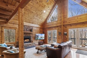 L’intérieur d’une cabane en rondins, avec une cheminée en pierre, un canapé en cuir et de grandes fenêtres.